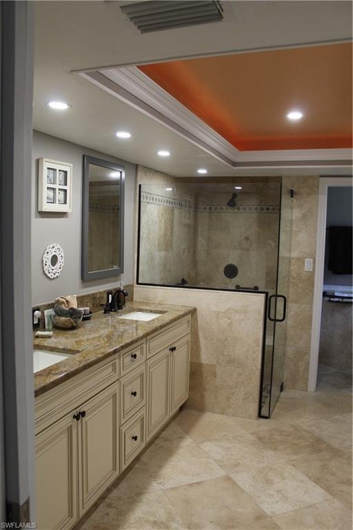 Full bathroom featuring a shower stall, a raised ceiling, double vanity, recessed lighting, and ornamental molding