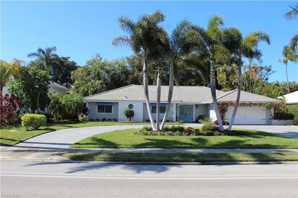 Ranch-style home featuring a front yard, covered porch, driveway, a garage, and stucco siding