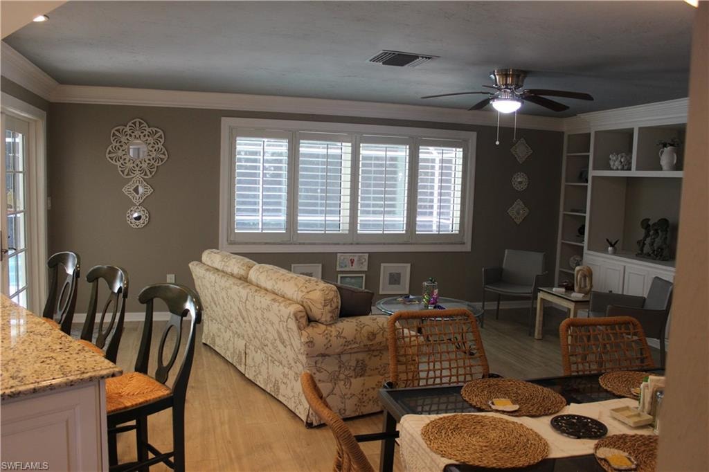 Living room featuring light wood-type flooring, ornamental molding, and ceiling fan