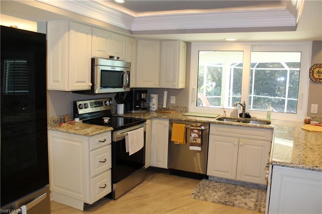 Kitchen with stainless steel appliances, light stone countertops, white cabinetry, a tray ceiling, and ornamental molding