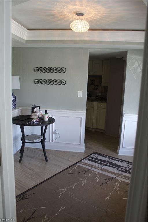 Hall with wainscoting, light wood finished floors, a decorative wall, and ornamental molding
