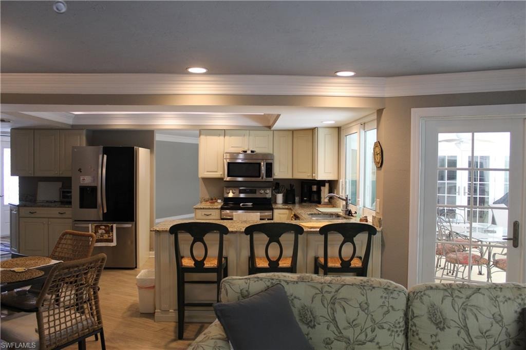 Kitchen featuring stainless steel appliances, a breakfast bar, light stone counters, light wood-style floors, and recessed lighting