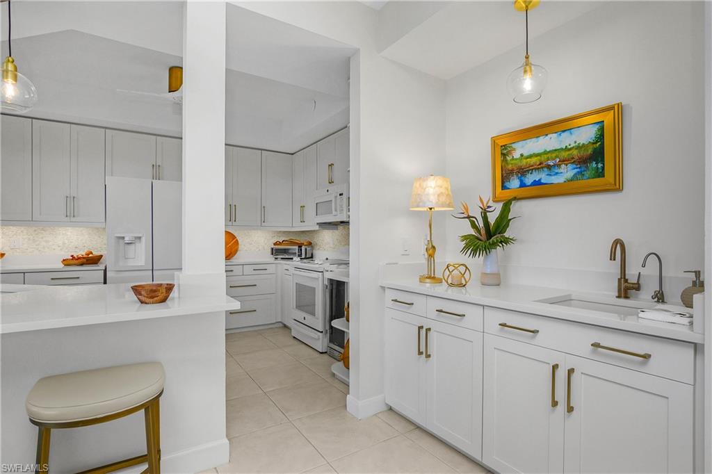 Kitchen featuring decorative light fixtures, white appliances, and light stone counters