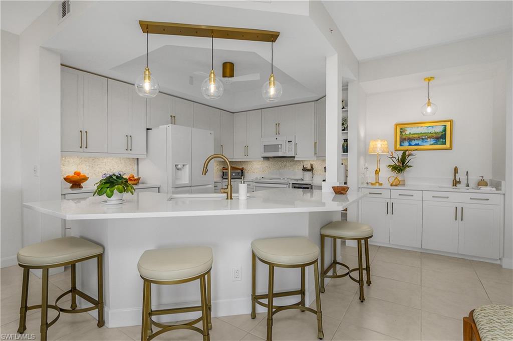 Kitchen with white cabinetry, backsplash, white appliances, decorative light fixtures, and a kitchen bar