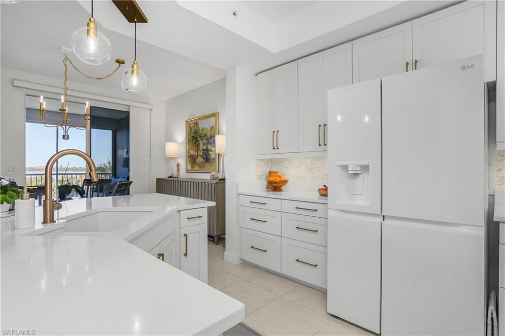Kitchen with white refrigerator with ice dispenser, white cabinets, decorative light fixtures, backsplash, and light tile patterned floors