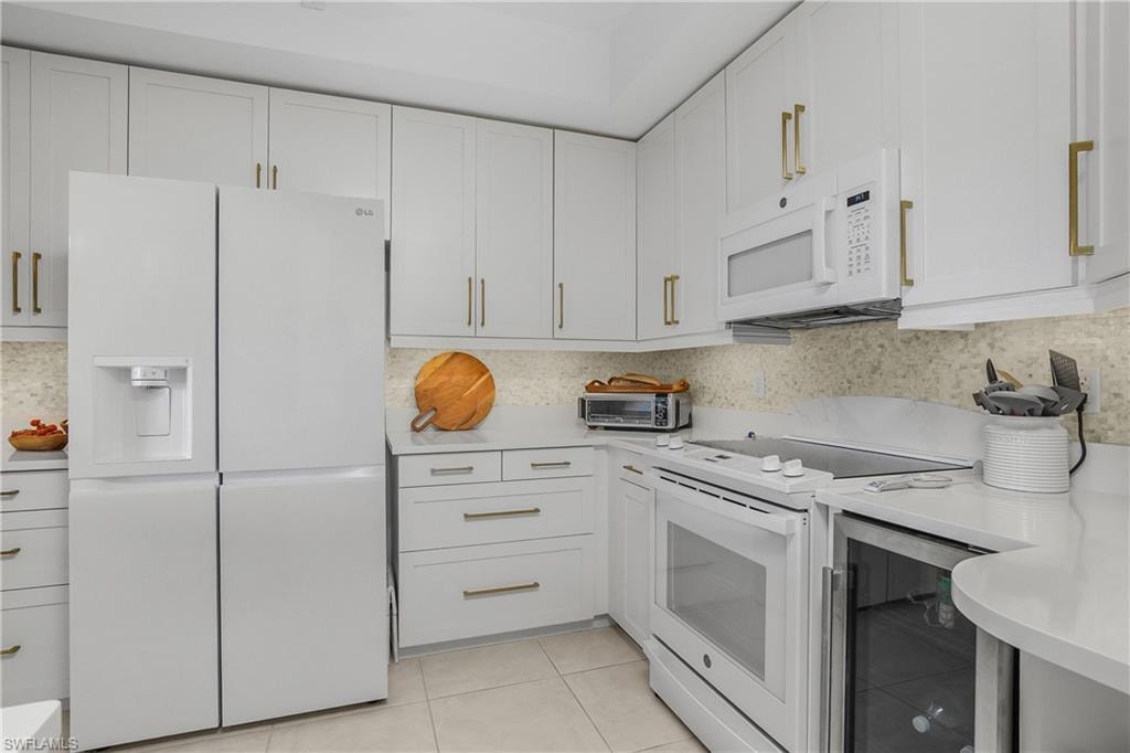 Kitchen with white appliances, beverage cooler, white cabinets, light tile patterned floors, and light stone counters