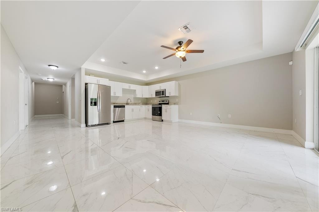 Unfurnished living room featuring a ceiling fan, a raised ceiling, recessed lighting, and light marble finish flooring