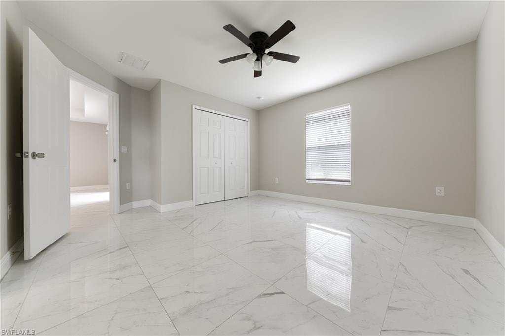 Unfurnished bedroom featuring a ceiling fan, light marble finish floors, and a closet