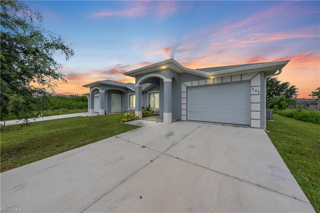 View of front of house with a yard, concrete driveway, stucco siding, and a garage