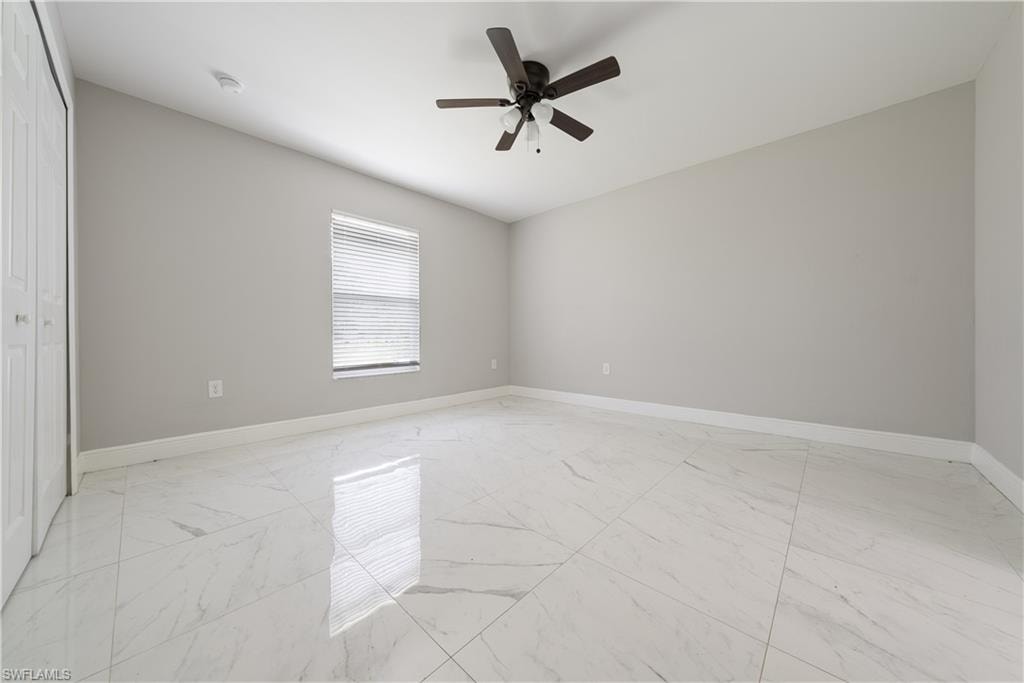Unfurnished bedroom featuring light marble finish flooring, a ceiling fan, and a closet