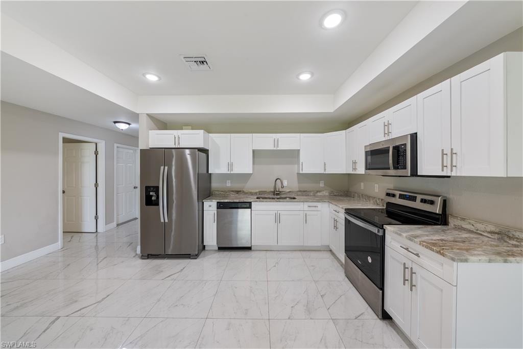 Kitchen with stainless steel appliances, white cabinets, light marble finish floors, and recessed lighting