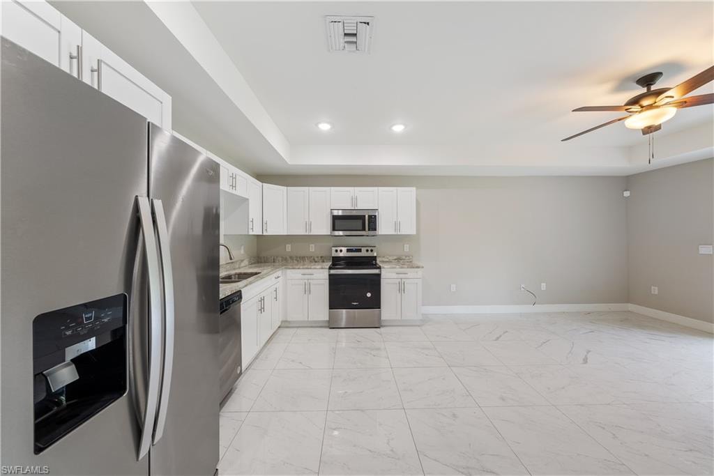 Kitchen with stainless steel appliances, a raised ceiling, a ceiling fan, white cabinets, and recessed lighting
