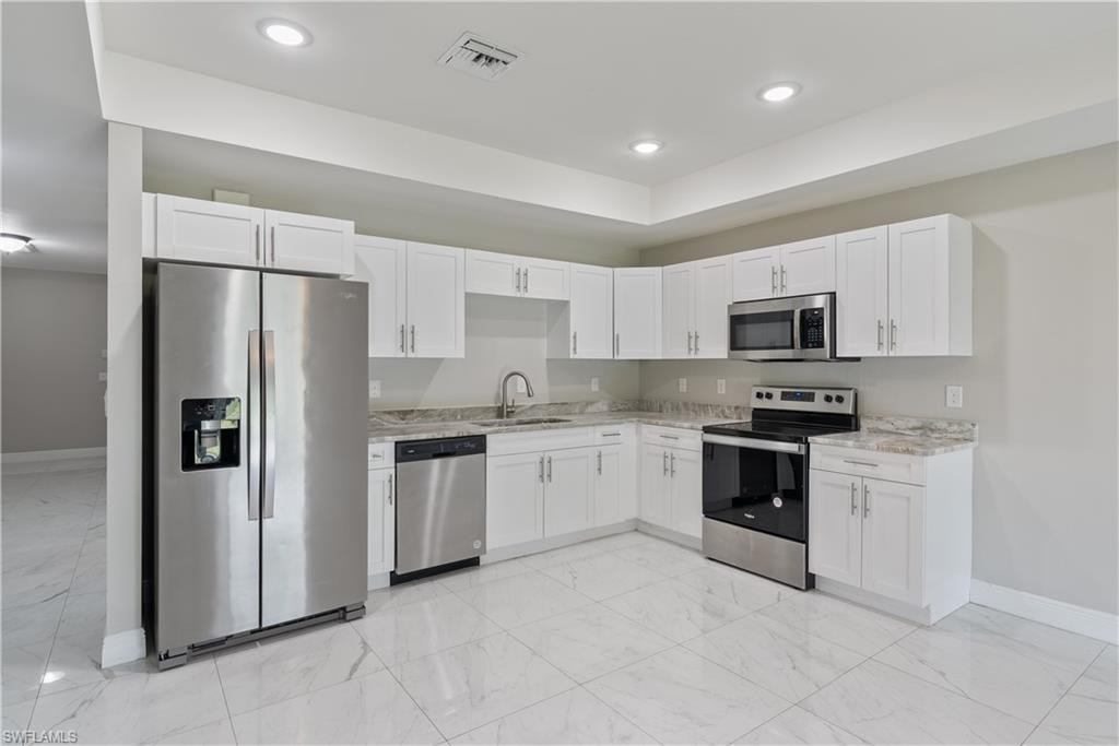 Kitchen with stainless steel appliances, white cabinets, light stone countertops, and recessed lighting