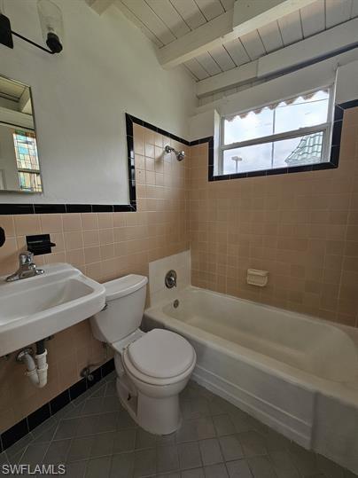 Bathroom with  shower combination, tile walls, light tile patterned floors, and a wood ceiling with exposed beams