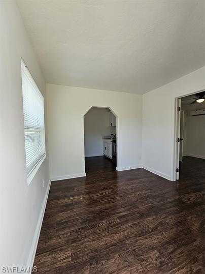 Spare room featuring dark wood-type flooring, ceiling fan, and arched walkways