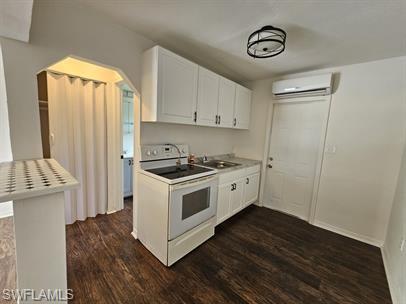 Kitchen featuring white range with electric stovetop, white cabinets, dark wood-style floors, and light countertops