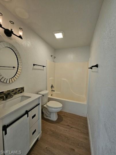 Full bath featuring a textured wall, vanity, dark wood-type flooring, and  shower combination