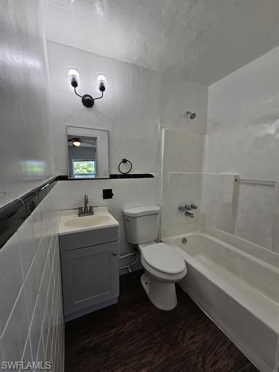 Bathroom with vanity, washtub / shower combination, dark wood-style floors, and tile walls