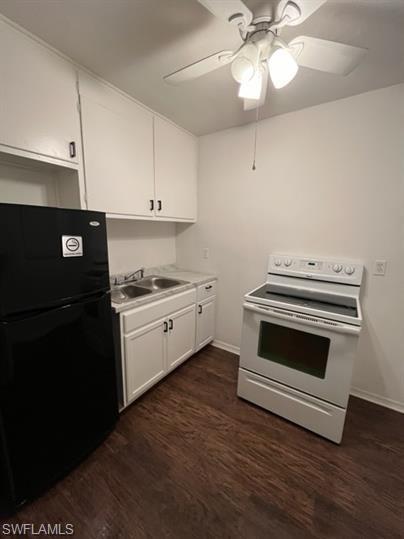 Kitchen featuring freestanding refrigerator, white range with electric cooktop, dark wood-style floors, white cabinets, and light countertops