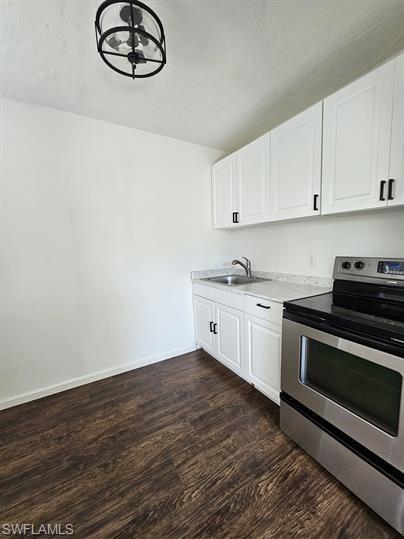 Kitchen with stainless steel electric range, white cabinetry, dark wood finished floors, and light countertops