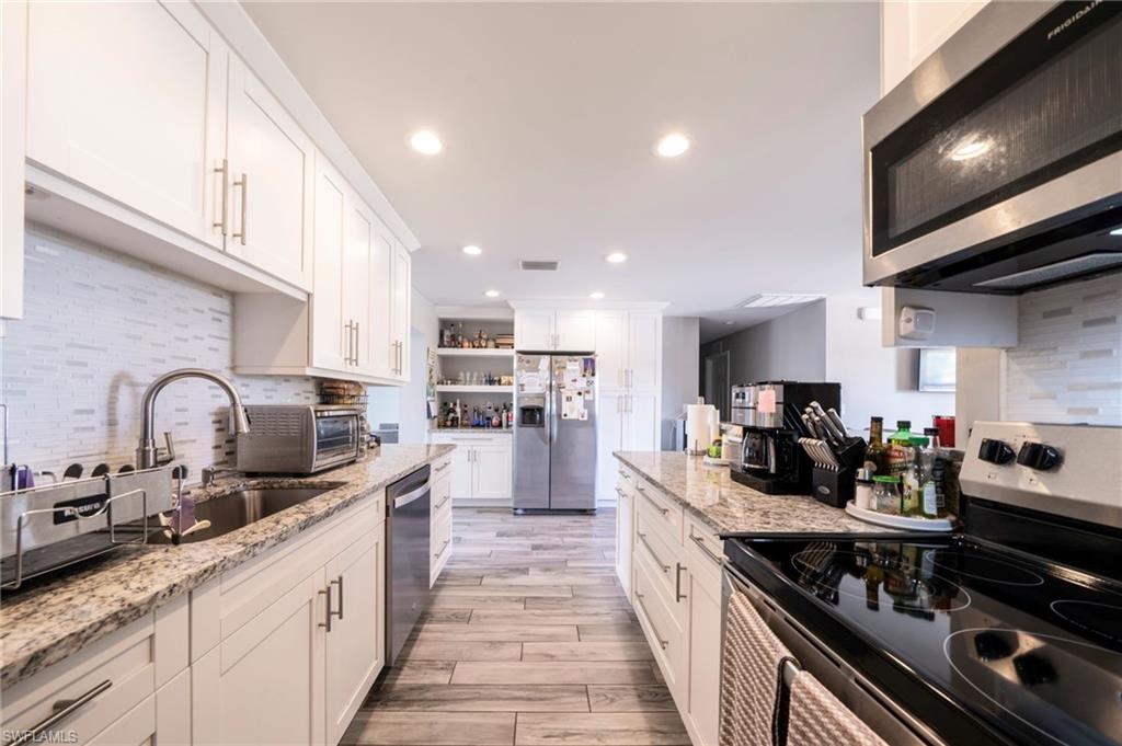 Kitchen with backsplash, stainless steel appliances, white cabinetry, light wood-type flooring, and light stone counters