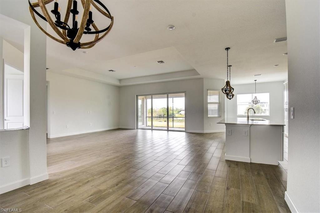 Unfurnished living room with suspended lighting, a tray ceiling, and dark wood-type flooring
