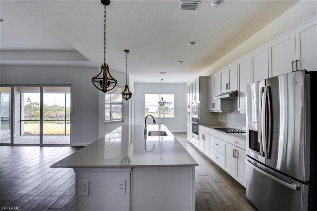Kitchen with stainless steel appliances, hanging light fixtures, an island with sink, dark wood-type flooring, and white cabinetry