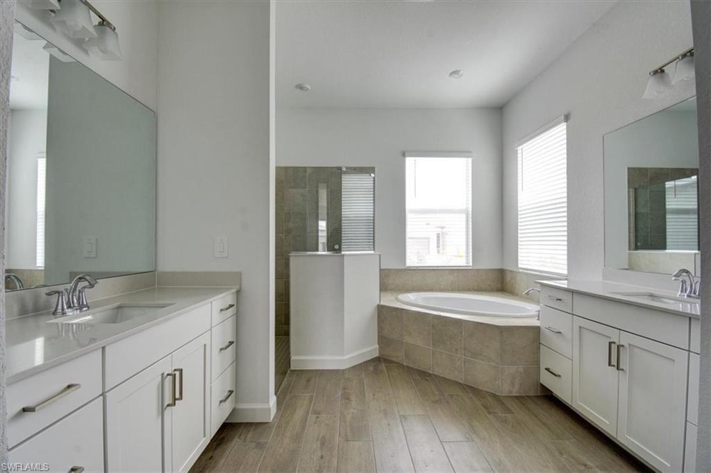 Full bathroom featuring two vanities, a bath, walk in shower, and light wood-type flooring