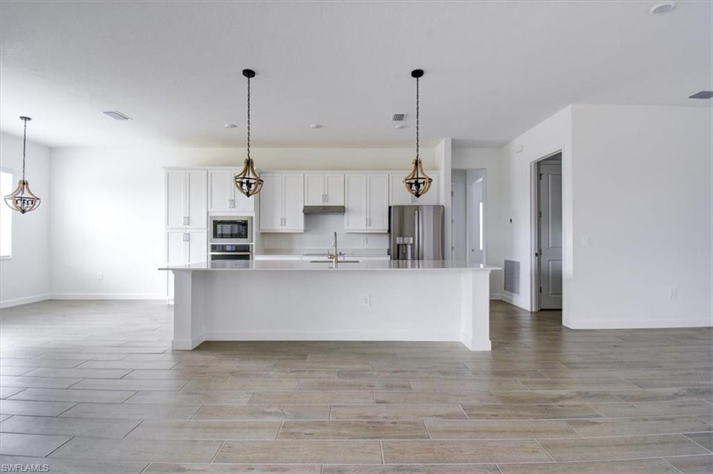 Kitchen featuring white cabinets, open floor plan, decorative light fixtures, stainless steel appliances, and a large island