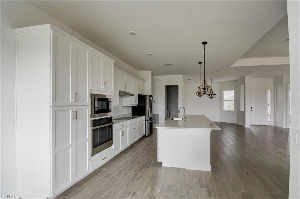 Kitchen with white cabinets, a center island with sink, stainless steel appliances, decorative light fixtures, and wood finish floors