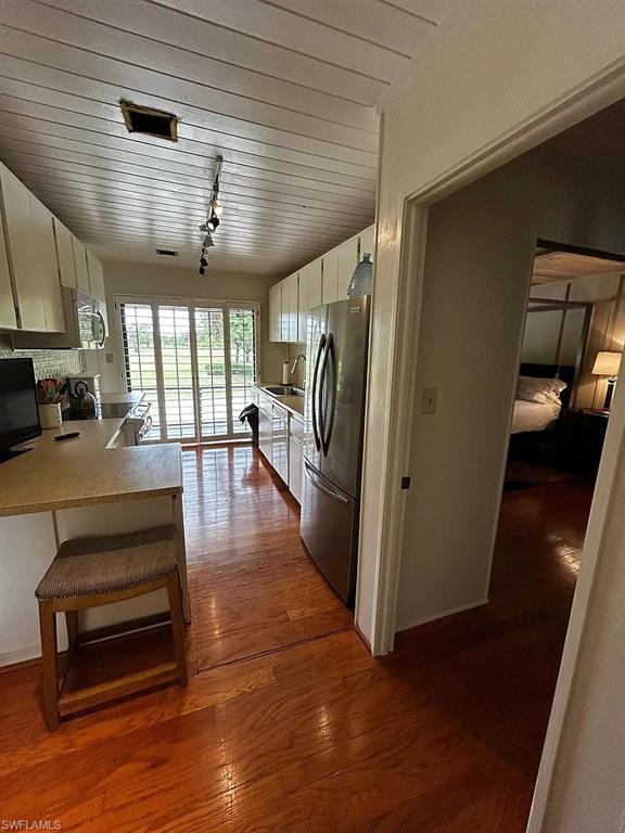 Kitchen featuring light countertops, dark wood finished floors, white cabinets, freestanding refrigerator, and a peninsula
