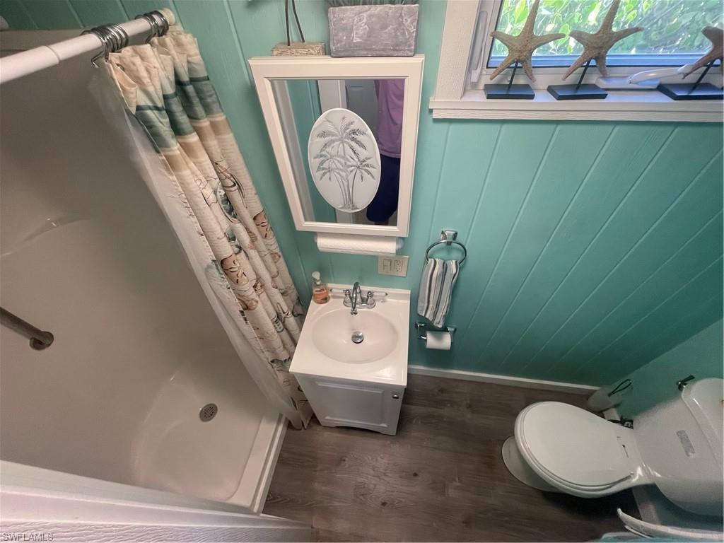 Full bathroom featuring curtained shower, wooden walls, and dark wood-style floors