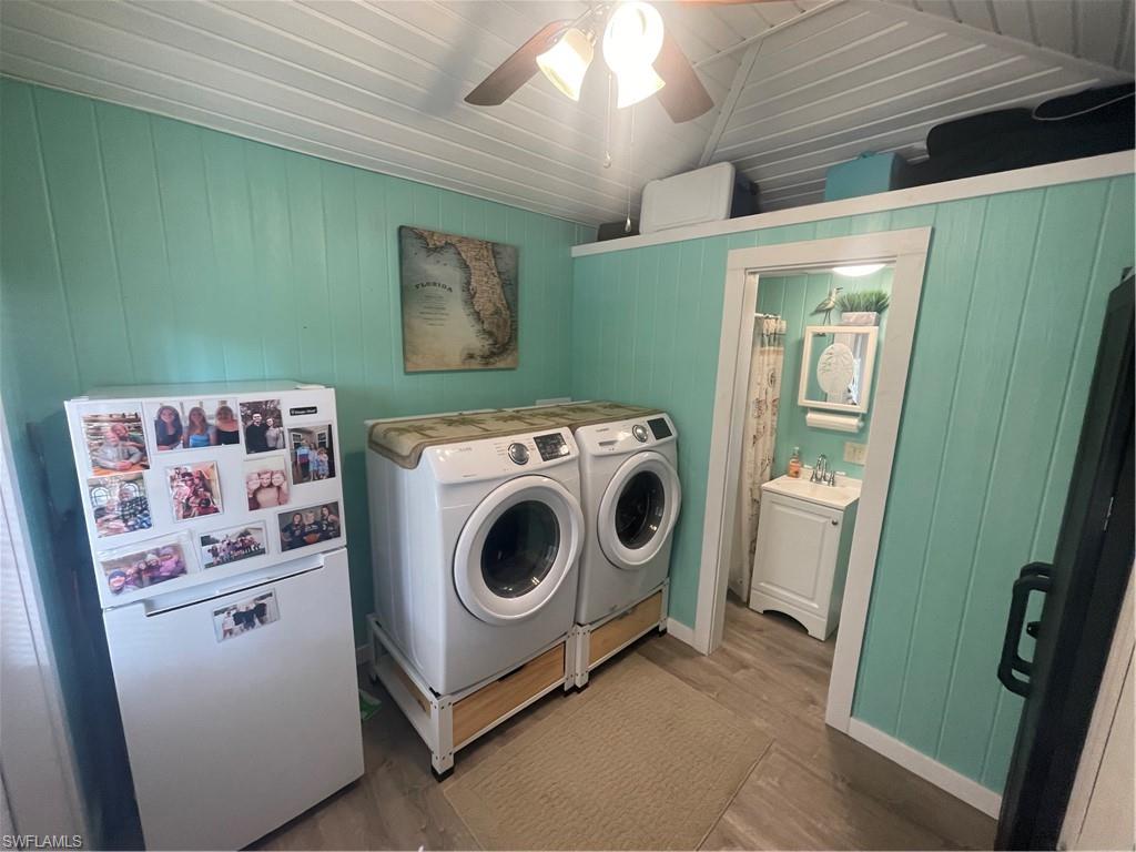 Laundry room with ceiling fan, washing machine and clothes dryer, wood finished floors, wooden walls, and lofted ceiling