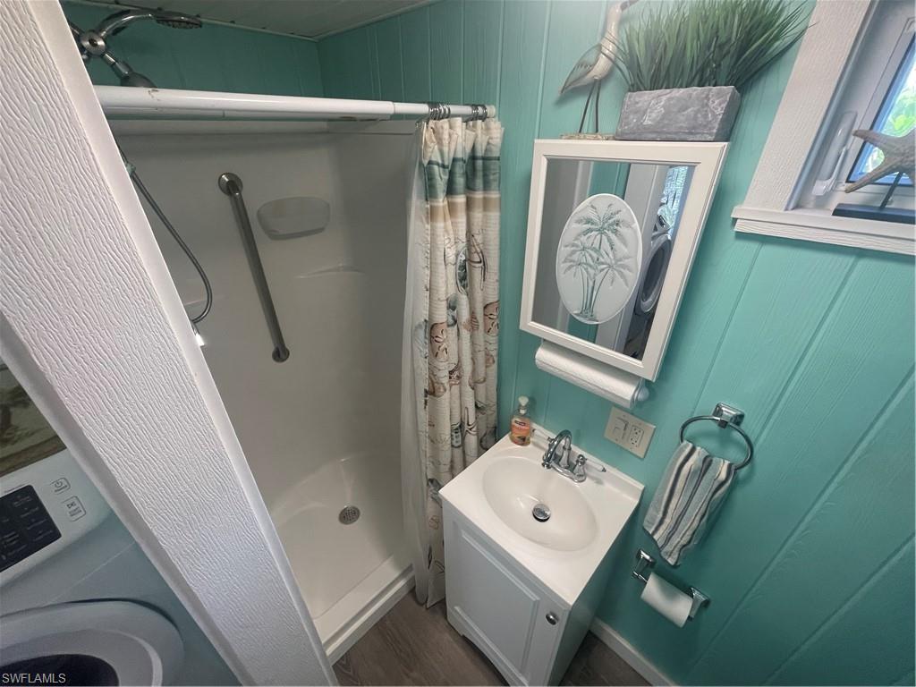 Bathroom featuring a stall shower, vanity, washer / clothes dryer, and wood walls