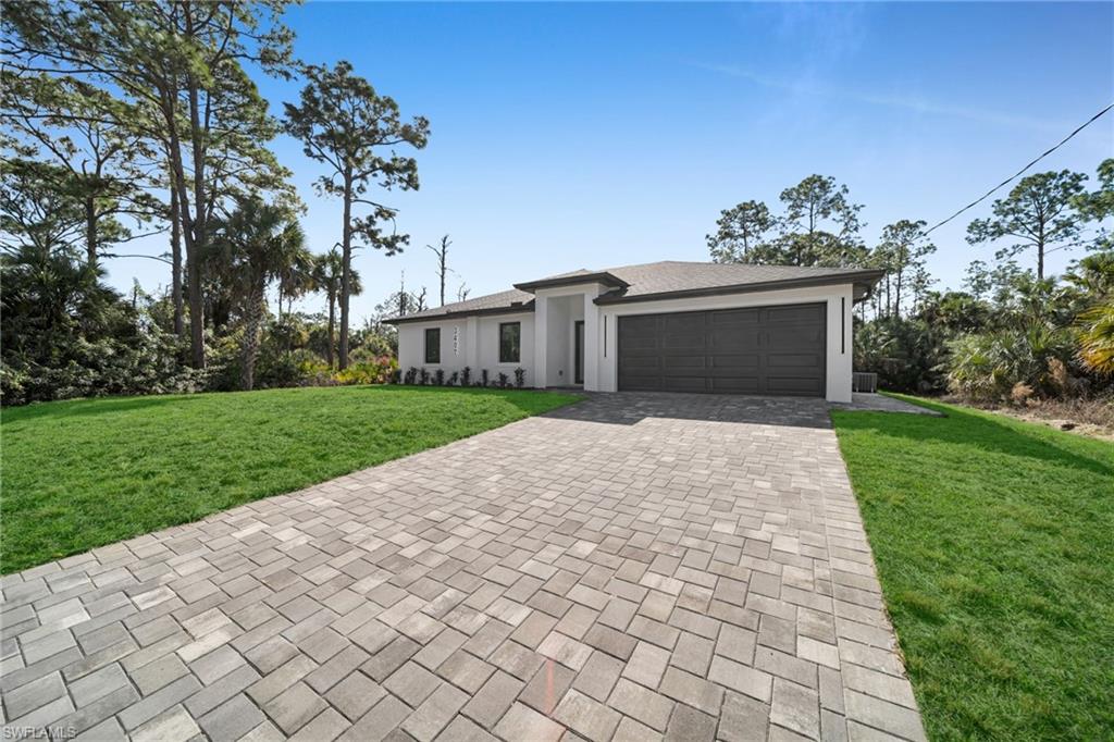 Prairie-style house with a front yard, decorative driveway, an attached garage, stucco siding, and a shingled roof