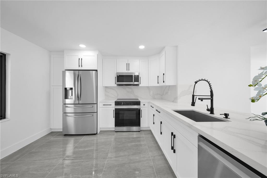 Kitchen featuring light stone counters, stainless steel appliances, white cabinets, decorative backsplash, and recessed lighting