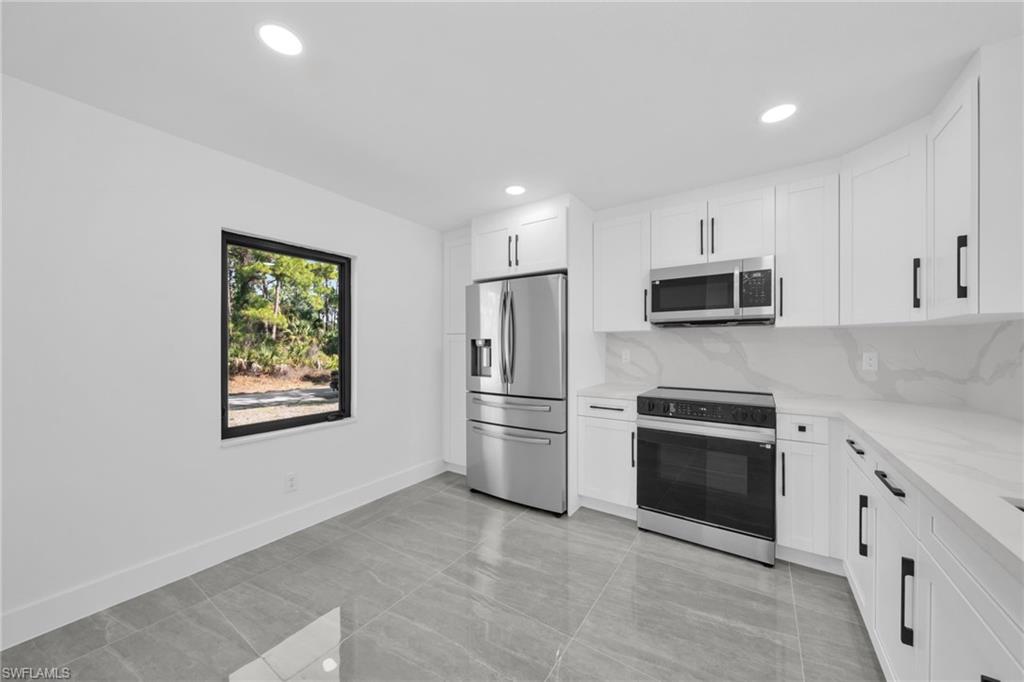 Kitchen featuring stainless steel appliances, white cabinets, light stone counters, backsplash, and recessed lighting