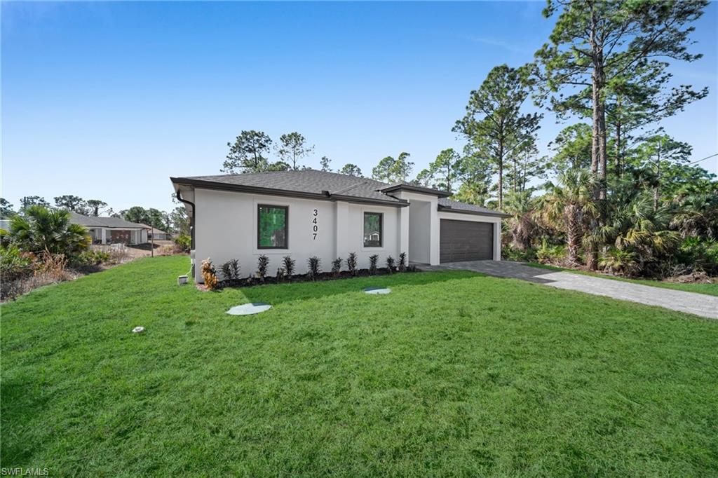 View of front facade with a front yard, driveway, stucco siding, and a garage