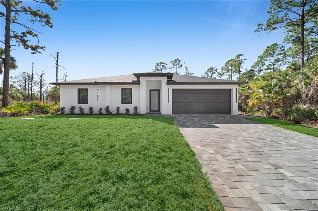Prairie-style home with stucco siding, decorative driveway, a front yard, and a garage