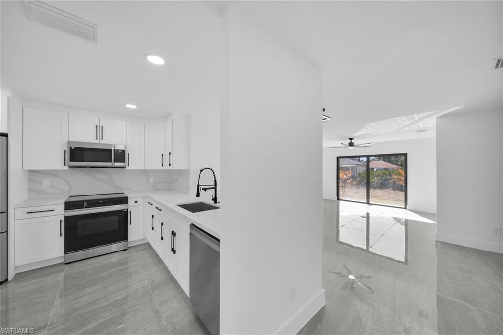 Kitchen featuring ceiling fan, white cabinets, stainless steel appliances, and light stone counters