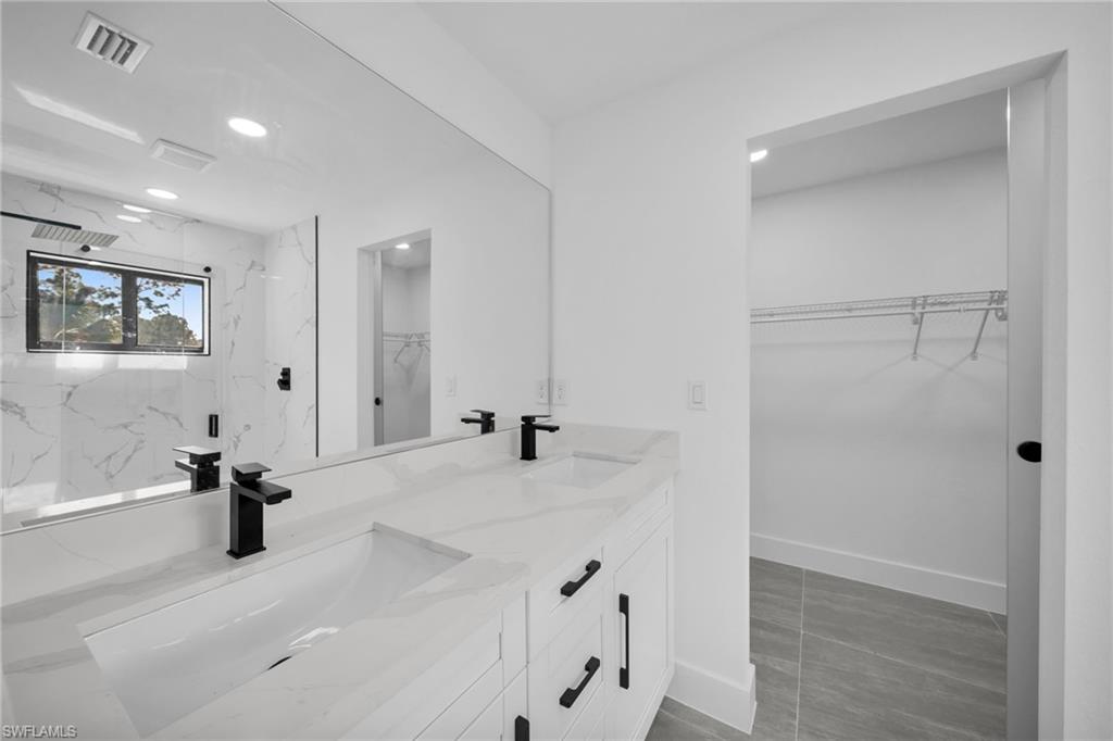 Full bath with a spacious closet, a marble finish shower, double vanity, and recessed lighting