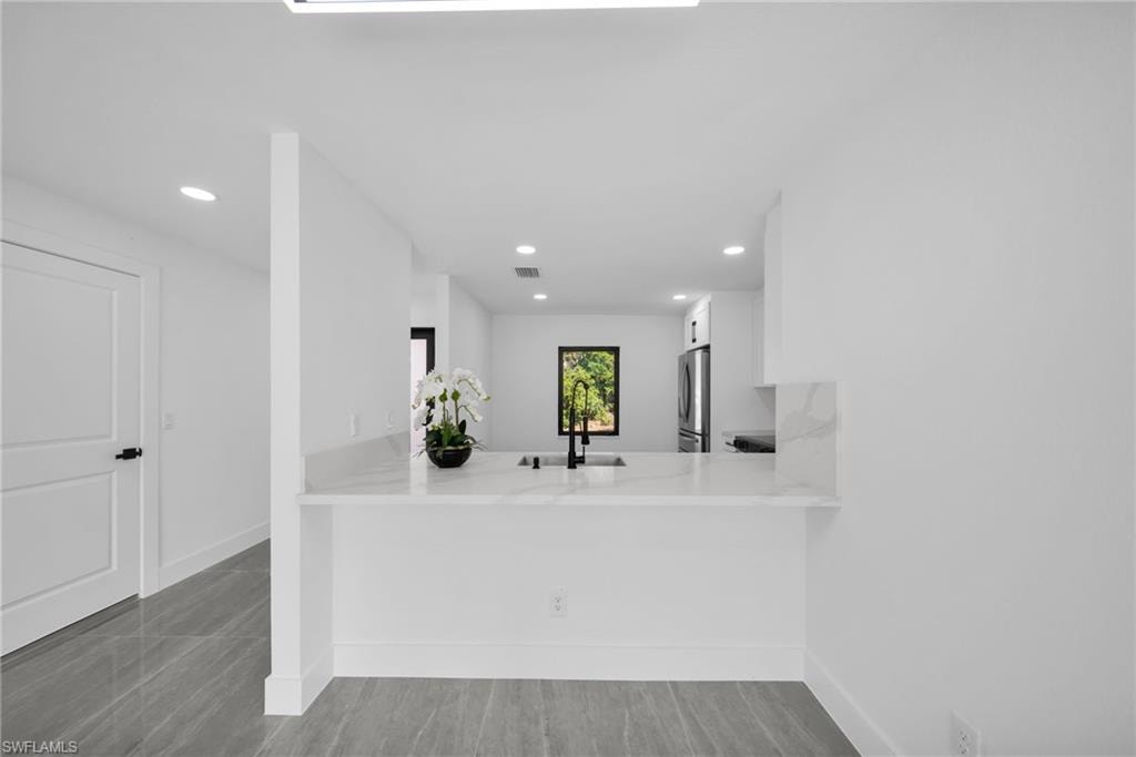 Kitchen featuring a peninsula, white cabinets, light stone counters, recessed lighting, and freestanding refrigerator
