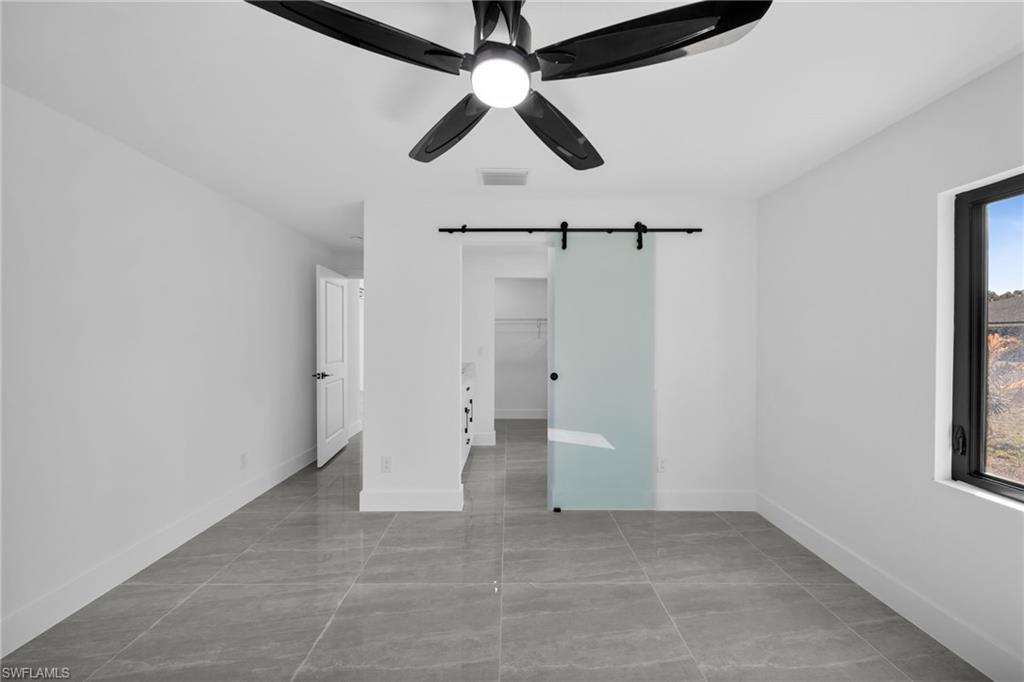 Unfurnished bedroom featuring a barn door, a walk in closet, and a ceiling fan