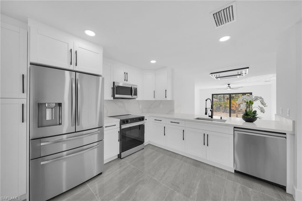 Kitchen with stainless steel appliances, white cabinetry, recessed lighting, light stone counters, and backsplash