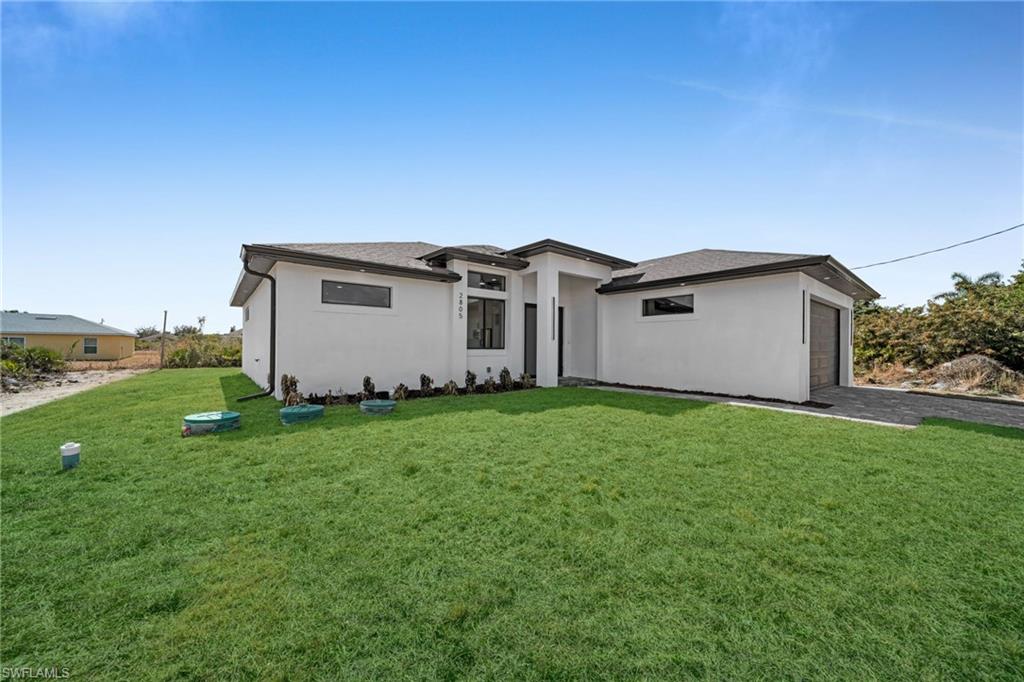 View of front of home with stucco siding, a front lawn, a shingled roof, driveway, and a garage