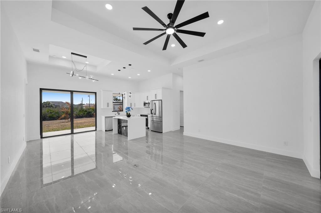 Unfurnished living room featuring a ceiling fan, a chandelier, and a raised ceiling
