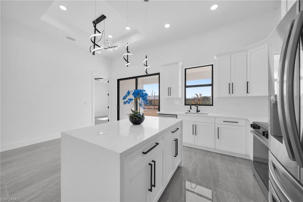 Kitchen with stainless steel appliances, white cabinets, a center island, hanging light fixtures, and a tray ceiling