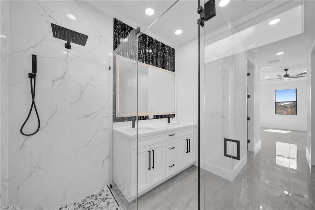 Full bath featuring a marble finish shower, double vanity, recessed lighting, and a ceiling fan