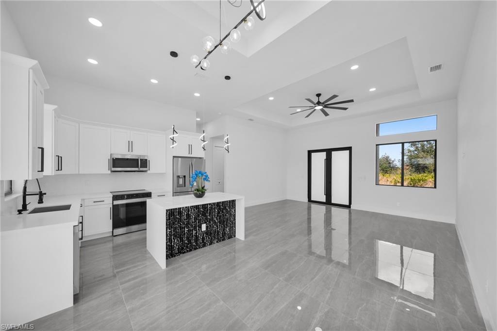 Kitchen with white cabinetry, stainless steel appliances, pendant lighting, light stone countertops, and open floor plan