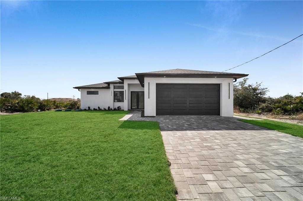 Prairie-style house with decorative driveway, stucco siding, a front lawn, and an attached garage